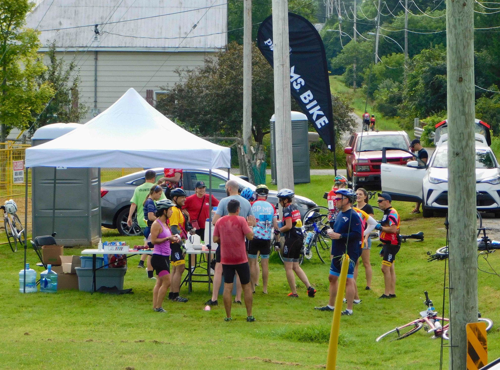 Cyclists and support volunteers gather around a tent in a field of grass